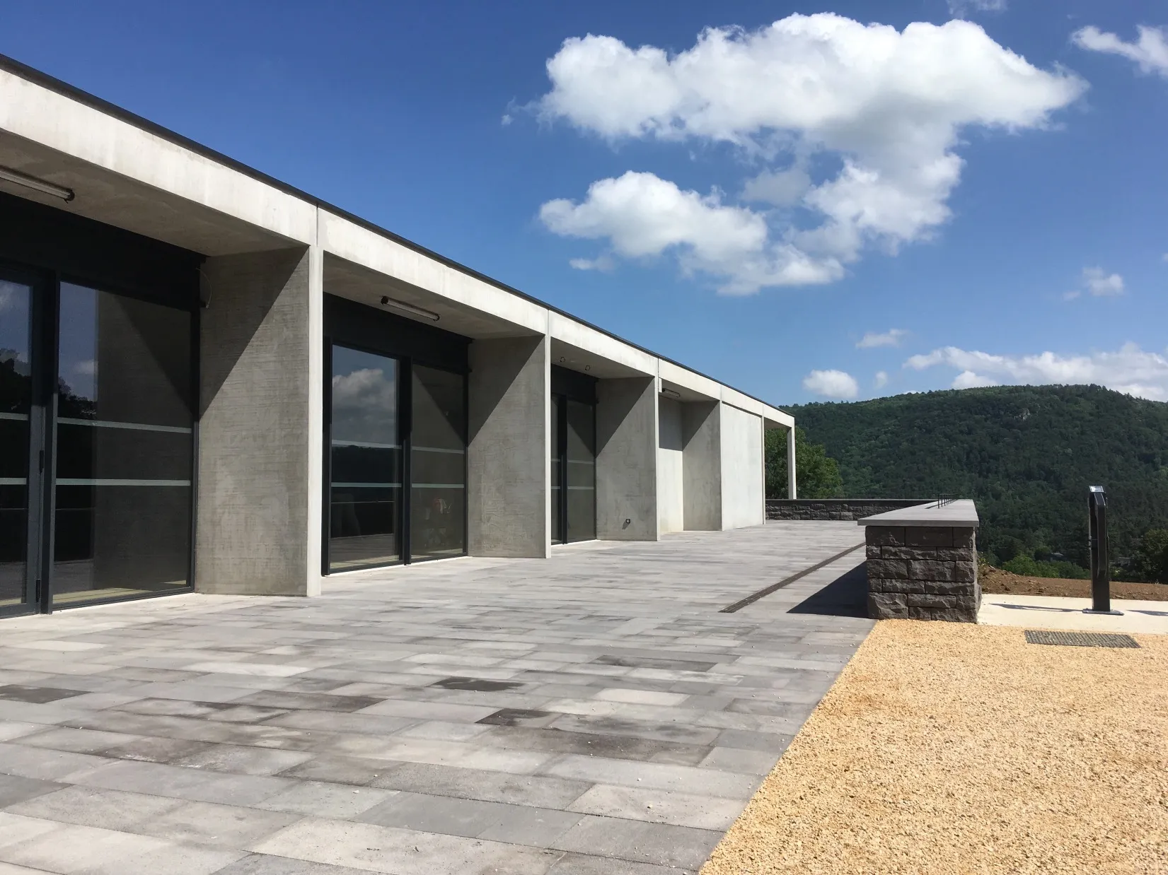 Bâtiment d'accueil du château de Murol : façade en béton et grandes baies vitrées ouvrant sur une esplanade en pierre, face aux monts d'Auvergne