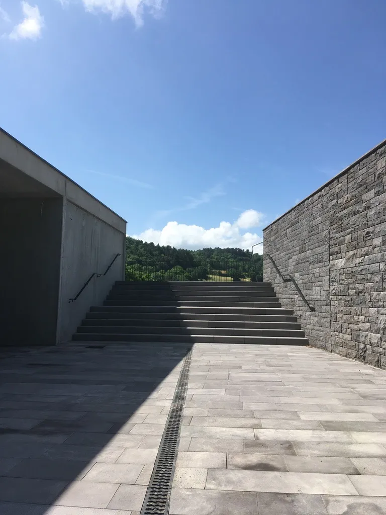 Escalier et parvis en pierre de l'accueil du château de Murol, entre mur en pierre volcanique et auvent en béton